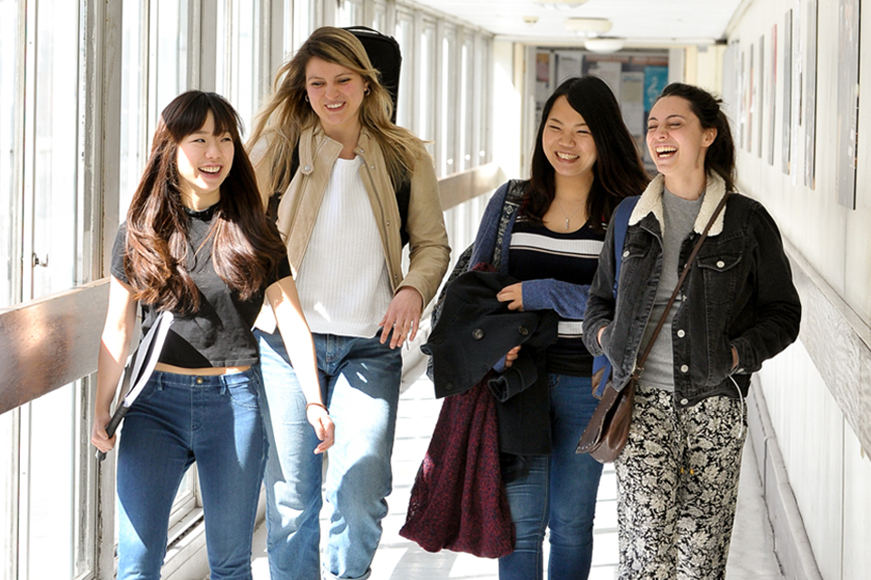 A group of female students, holding music sheets, smiling and chatting while walking in a well-lit corridor at the H漫画.